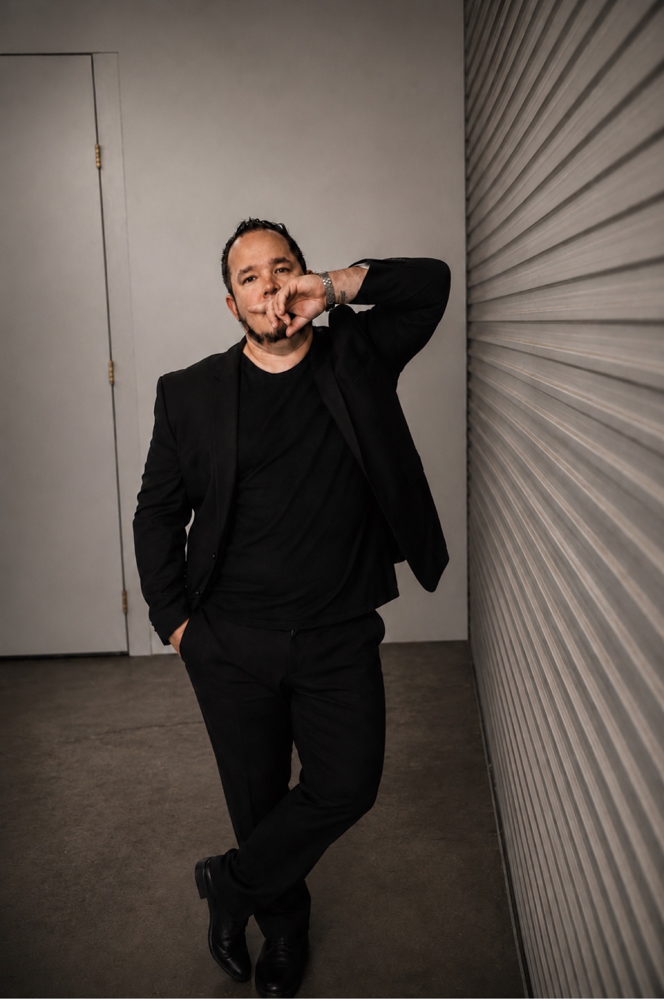 Emad Alayoubi in a black suit leaning against a shutter